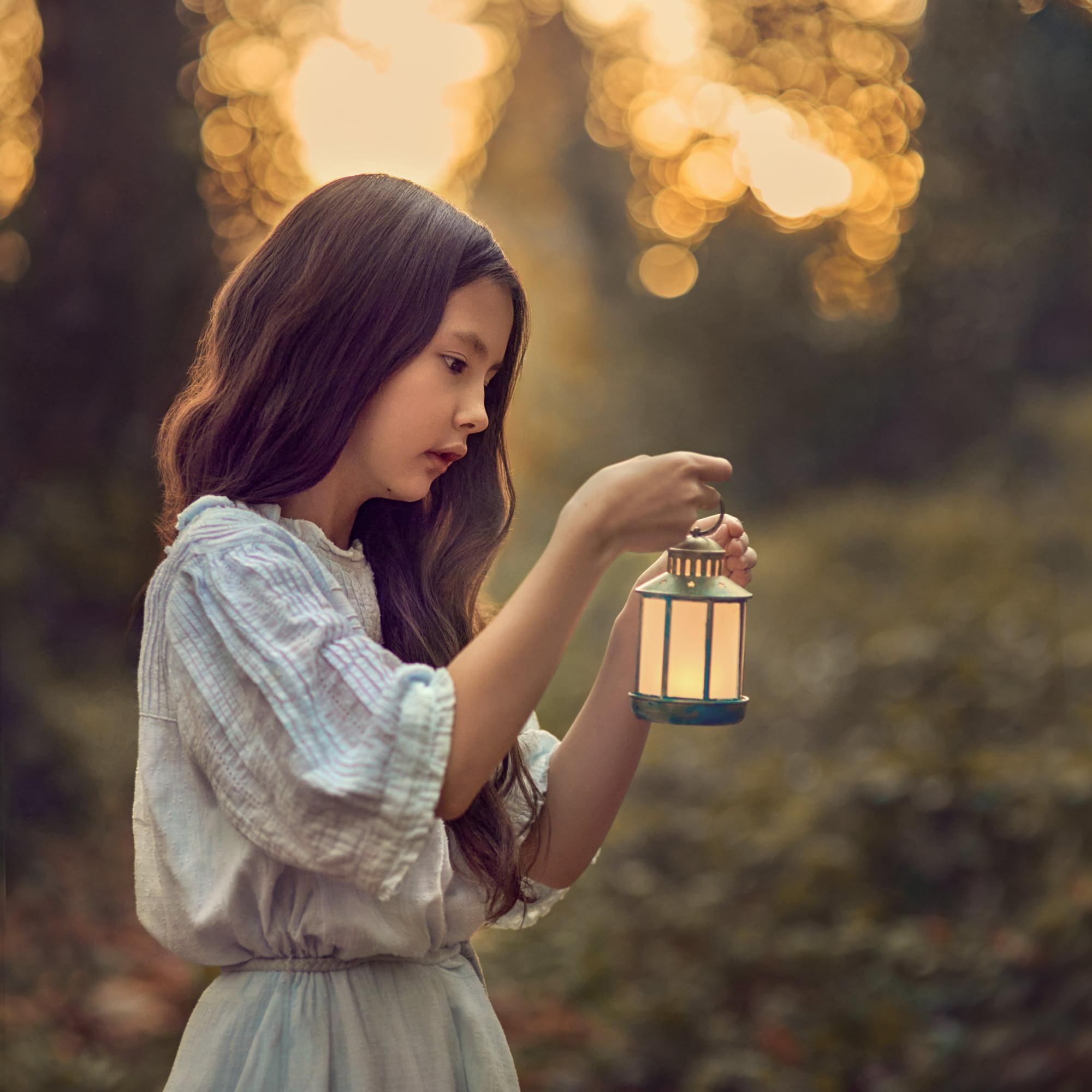 Dreamy portrait of a girl holding a lantern at sunset in the autumn woods.