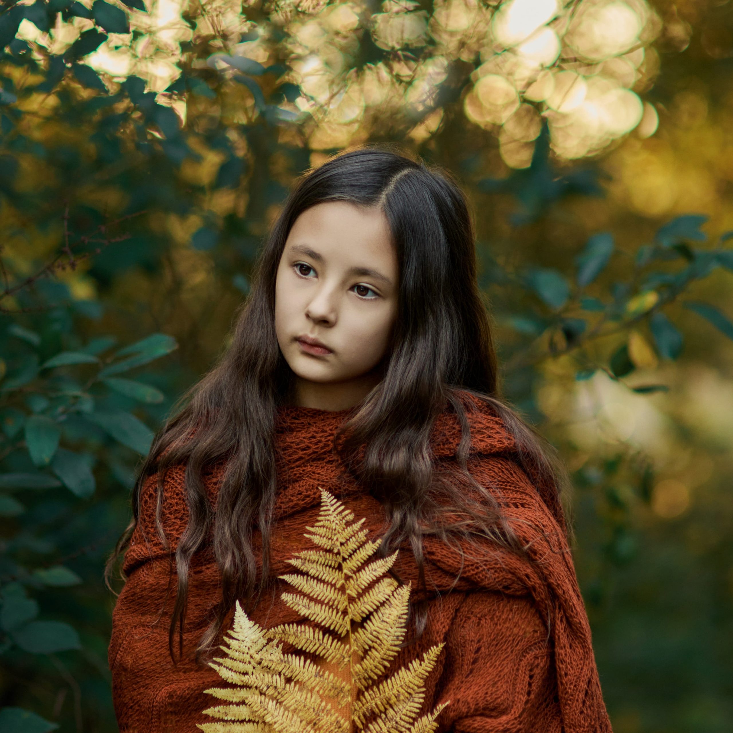 Dreamy fine art portrait of a child holding a fern in autumn woods.