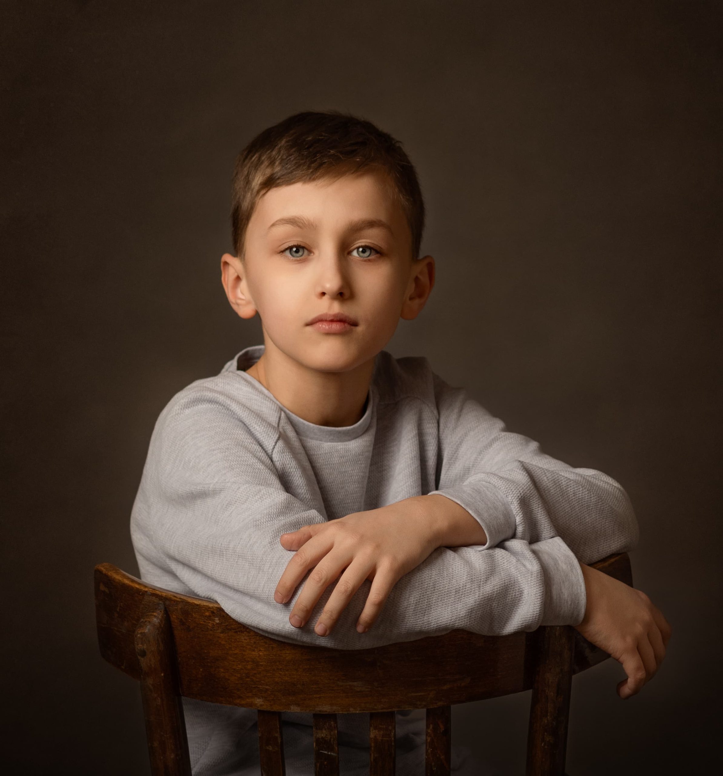 Fine art portrait of a boy sitting on a chair in low-key classic Dutch painting style.